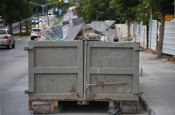 Back view of metal Roll off (dumpster) full of construction waste in the street near a construction site.    