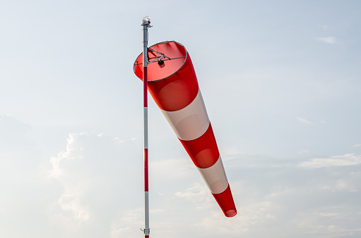 Red and white windsock inflated by the wind blows against a blue sky