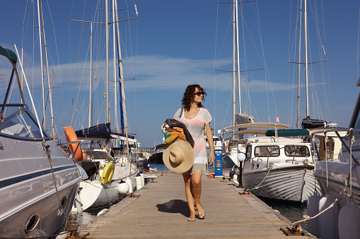 young woman walking in yacht marina with beach dress