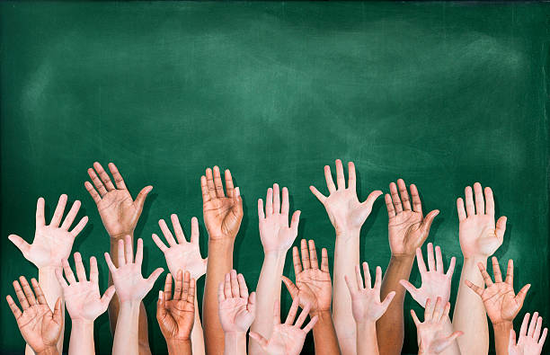 Diverse raised hands in front of blackboard A multi-ethnic group of students' hands raised in front of a classroom blackboard.  There are 18 hands raised, visible to the wrist or elbow, and seen from the side of the palm.  The blackboard is dark green and has been freshly erased. hand raised classroom student high school student stock pictures, royalty-free photos & images