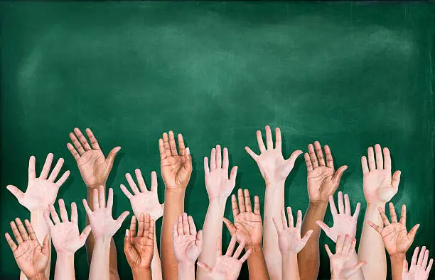 Photo of Diverse raised hands in front of blackboard