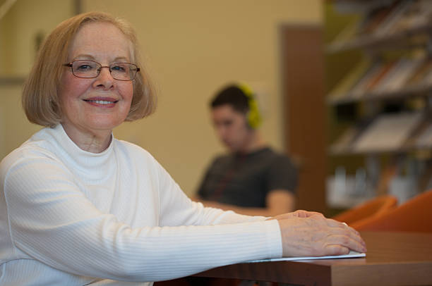 istock Senior woman at library sitting at table with book 488869437