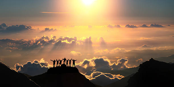 On the top of the world together A group of people standing on a hill over the beautiful cloudscape. group mountain silhouette stock pictures, royalty-free photos & images