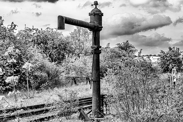 A railway station is closed. Nature is reclaiming its place. Old railway tracks are overgrown. A water pump for steam locomotives stands lonely in the landscape and rusted.