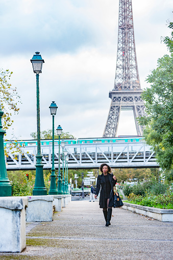 Stylish young African woman walking in Paris wit the Eiffel Tower and a metro train