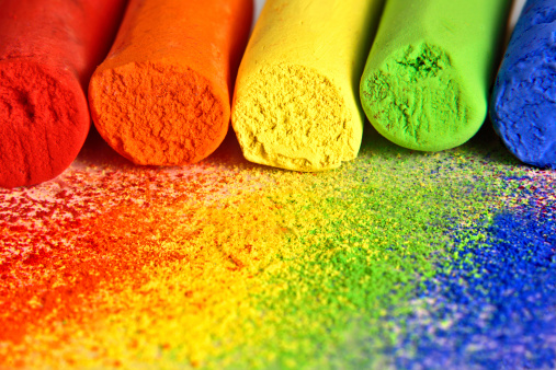 Macro of pastel chalk sticks in a rainbow of colors with their powders in front.