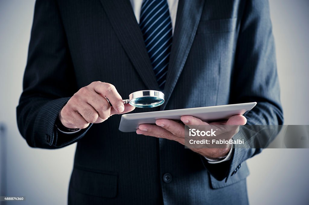 Businessman holding magnifying glass and digital tablet Identity Stock Photo