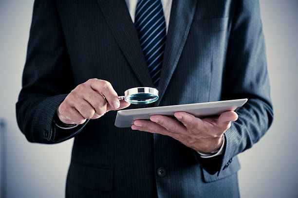 Businessman holding magnifying glass and digital tablet stock photo
