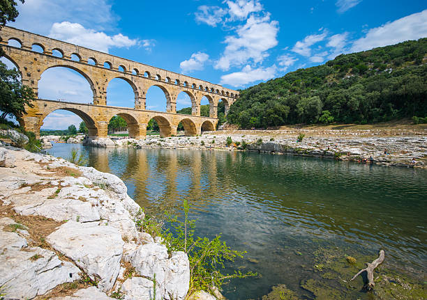 The photo is  HDR (high dynamic range) obtained by combining several images with different exposure time.  The Pont du Gard is a notable ancient Roman aqueduct bridge that crosses the Gard River in southern France. It is part of a 50 km (31 mi) long aqueduct that runs between Uzes and Nimes in the South of France.