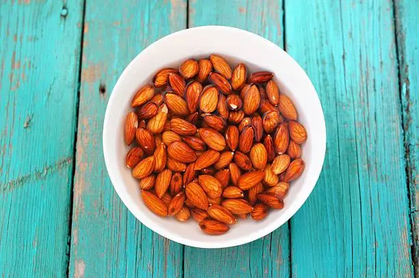 Photo of Wet raw almonds on turquoise wooden table