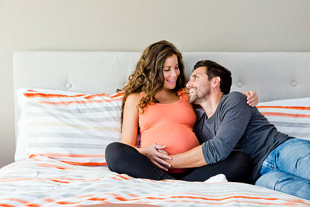 妊娠中のカップルのベッドの上に座る - bed cheerful enjoyment excitement ストックフォトと画像