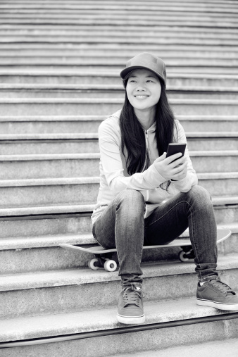 young woman skateboarder use her cell phone sit on stairs