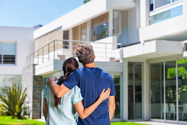 Cople family looking to new modern big house couple embracing in front of new big modern house, outdoor rear view back looking at their dream home common couple men outdoors stock pictures, royalty-free photos & images