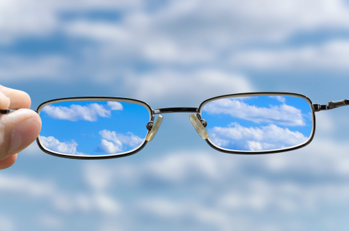 out of focus sky with hand holding a glasses that correct the vision