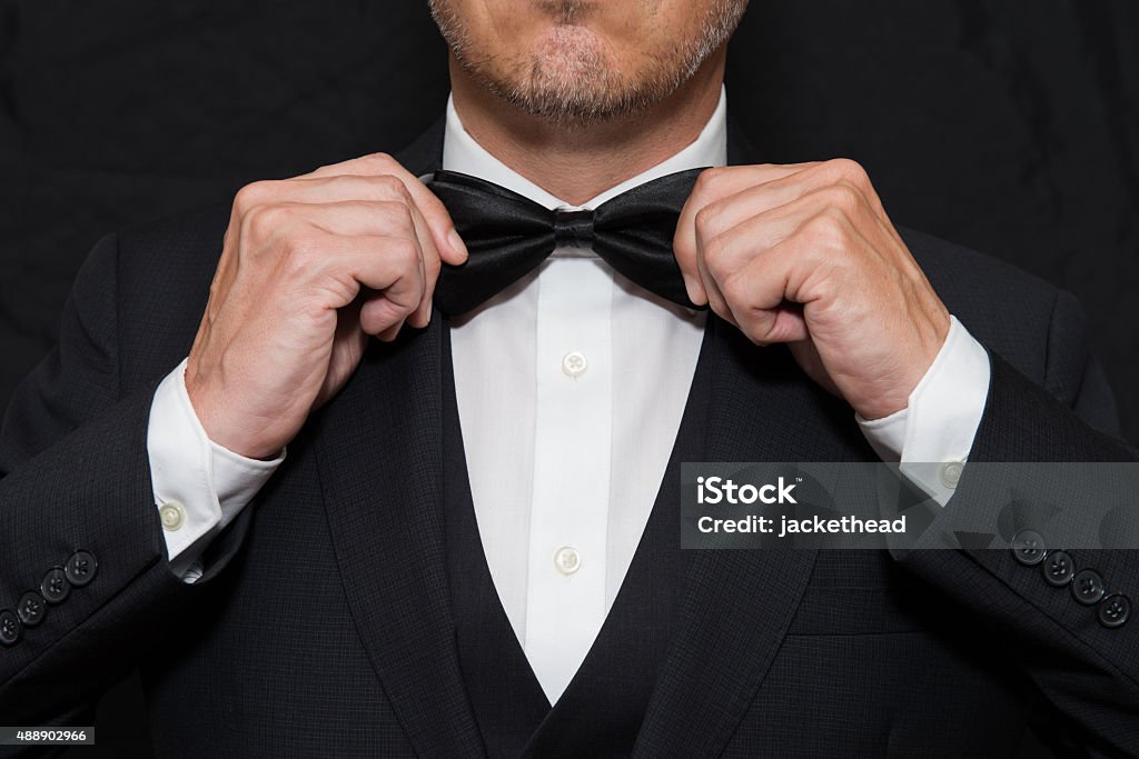 Gentleman in Black Tie Straightens His Bowtie Close-up of a gentleman wearing Black Tie straightens his bowtie. Formalwear Stock Photo