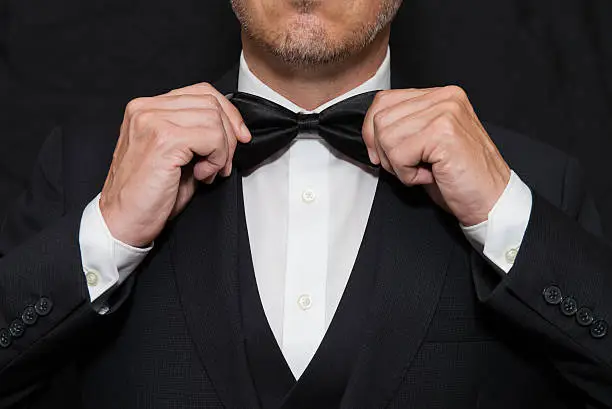 Photo of Gentleman in Black Tie Straightens His Bowtie