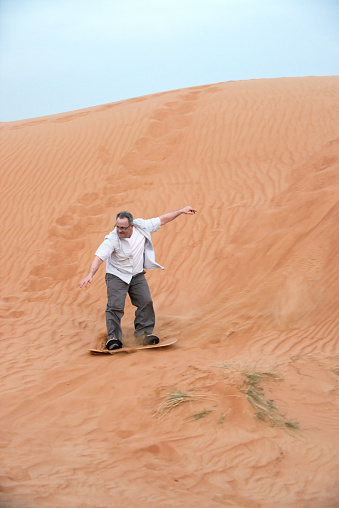 Dubai iStockalypse.  A mature Caucasian man, solo adventure tourist sandboarding down a sand dune in the red desert between Dubai and Sharjah, United Arab Emirates.  Closeup view with copyspace.