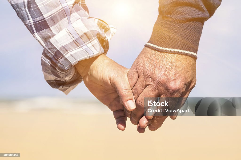 Senior couple in love walking at the beach holding hands Senior couple in love walking at the beach holding hands in a romantic sunny day - Concept of love and family union Senior Couple Stock Photo