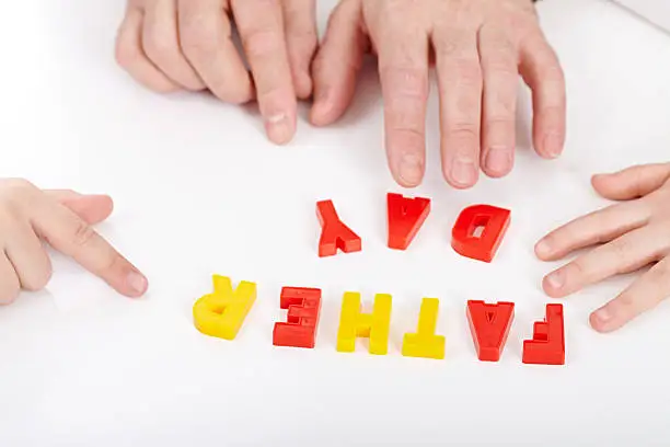 Hands of father and two children making FATHER DAY from plastic alphabet letters