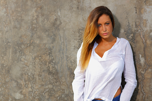 Stock photo of a young woman leaning on a wall in a white shirt