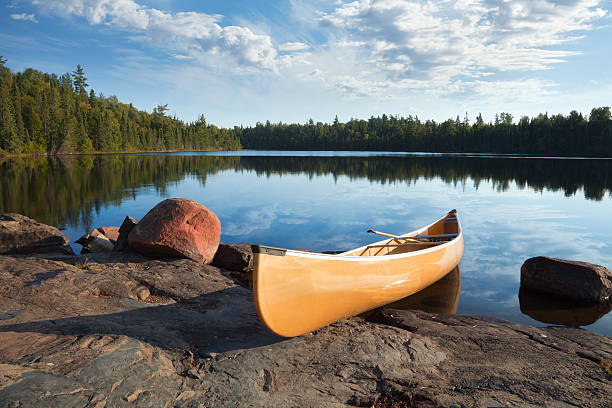 canoe on rocky shore de calma lago de pinos - canoeing canoe minnesota lake fotografías e imágenes de stock