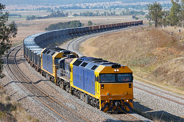 Train of containers loaded with ore rounding a curve Three diesel-electric locomotives work hard uphill and around an s-curve with a trainload of containerised ore on its way from mine to port.  Two large locomotives with a small one in the middle – all identification marks and logos removed.  Unidentifiable people. freight train stock pictures, royalty-free photos & images
