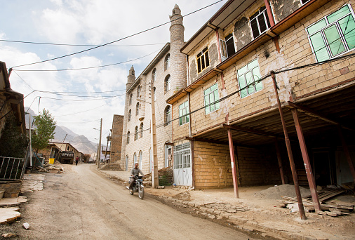 Hawraman-e Takht, Iran - October 10, 2014: Motorcycle driver goes past the brick houses of iranian village in mountains on October 10, 2014. Islamic Republic of Iran is the world's 17th most populous nation 