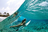 Over/under of surfer girl duck diving tropical waves