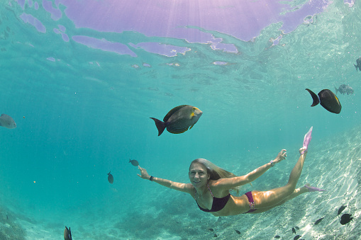 A girl looks at a fish swimming by underwater while in a tropical lagoon.