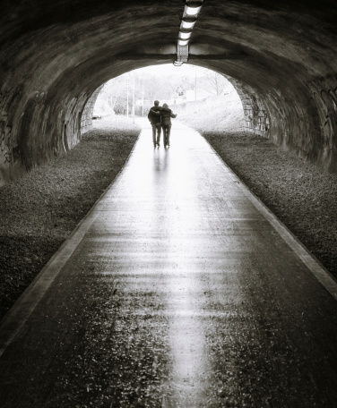 Black and white image of an adult couple silhouetted against daylight at the end of a long tunnel.  Model released image.