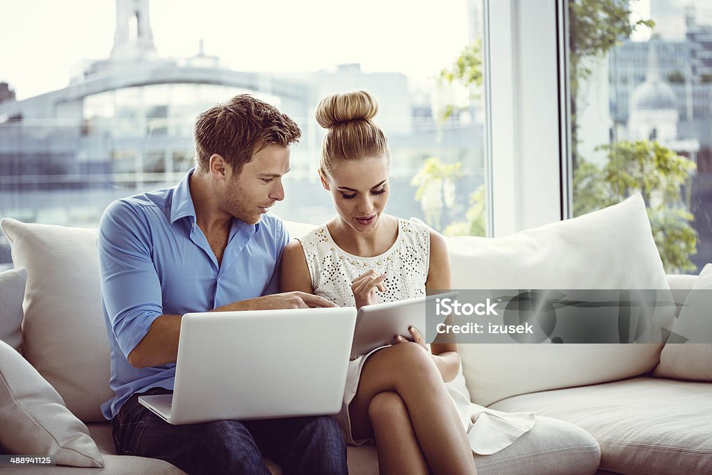 Couple with technologies Young couple sitting on sofa in an apartment and using digital tablet and laptop together. Luxury Stock Photo