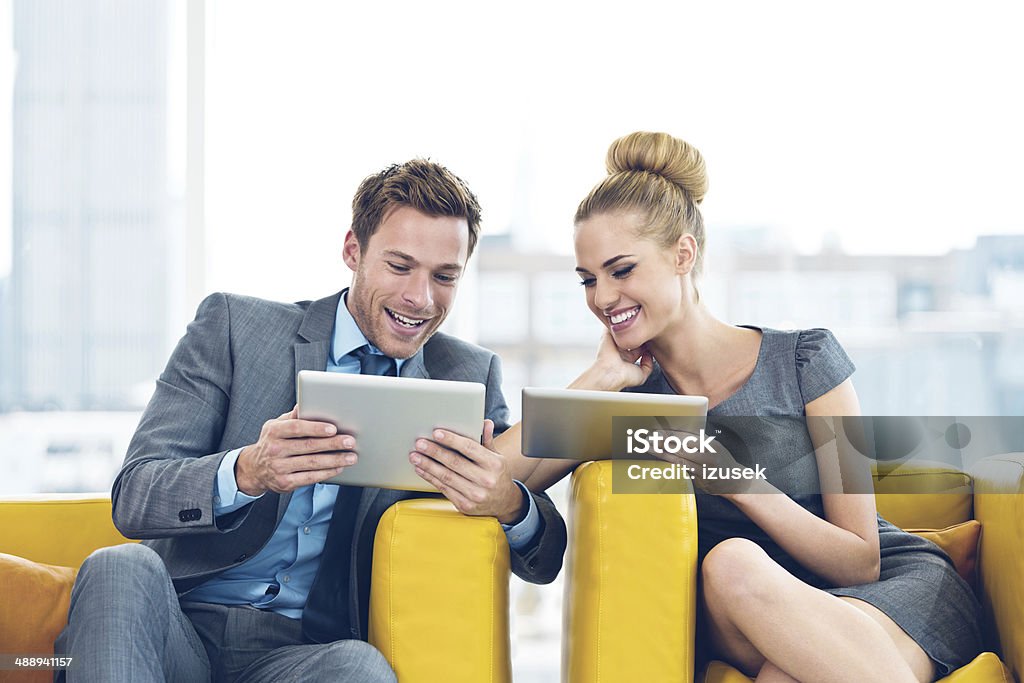 Business people with digital tablets Businessman and businesswoman sitting in chairs and checking their agendas on digital tablets. Office Stock Photo