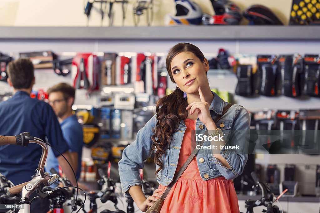 Young woman in bike store Portrait of pensive young woman standing in bike store  with two men in the background. Buying Stock Photo
