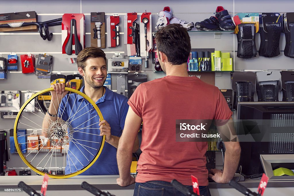 Bike store Sales clerk holding a bicycle wheel and talking with customer in bike store. Bicycle Stock Photo