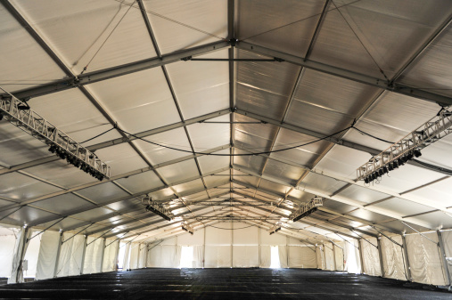 Large white tent with black floor and rafters and lighting ready for a party