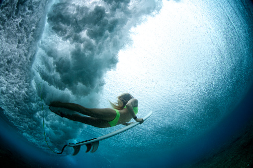 A girl duck dives a wave from underneath into the light