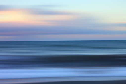 Abstract landscape with blurred motion and moody colors. Seascape background at dawn, with textured sea water, blurred sky before the sun comes up. Dreamlike effect with dark blue hues and pastel colors. Blue and yellow colors.