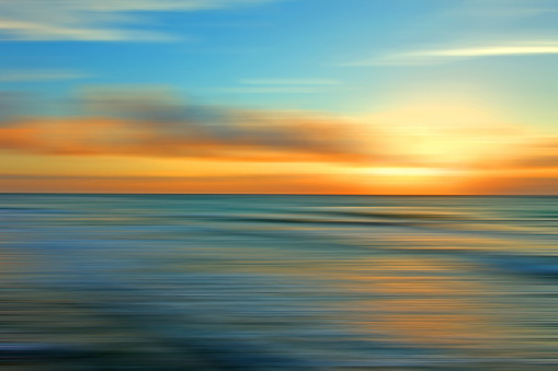 Abstract landscape with blurred motion. Seascape at sunset, with textured sea water, blurred sky and warm sunlight. Dreamlike effect with soft hues and pastel colors, ethereal sky and multi colored reflections. Blue, yellow and orange colors.