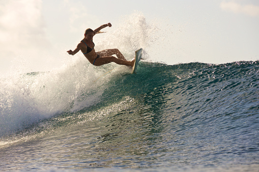 A surfer girl does a big turn on a breaking wave in a bikini
