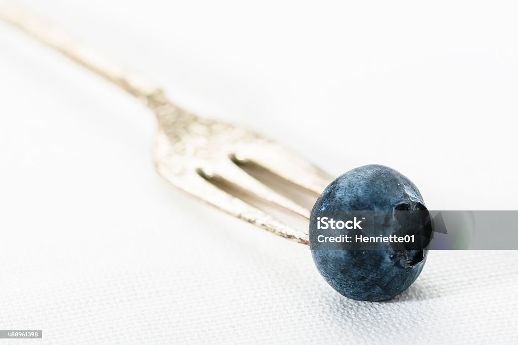 Singe blueberry on a silver fork A close up of a single blueberry on a silver fruitfork on a white tablecloth 2015 Stock Photo
