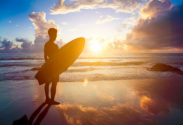 istock surfer man standing on beach and holding a surfboard 488964553