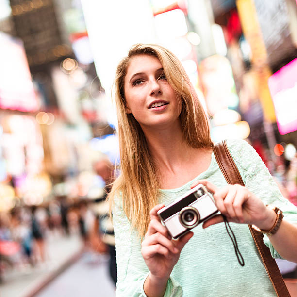 istock pretty woman smiling on times square with camera 488975128