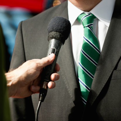 Portrait of a happy businessman answering questions to a media reporter with a microphone in her hand