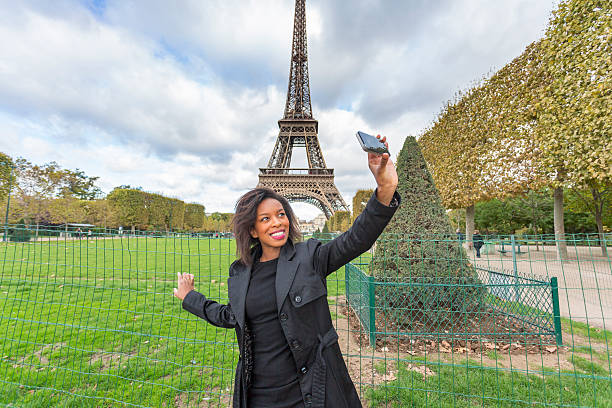 Happy and stylish young African woman taking a selfie self portrait in Paris with the Eiffel Tower