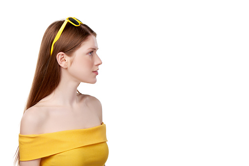 Closeup profile of calm redheaded female wearing bright yellow strapless top and yellow sunglasses looking forward, over white background