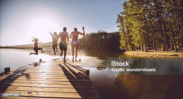 Four People Jumping Off A Jetty Into The Water Stock Photo - Download Image Now - Lake, Jumping, Swimming