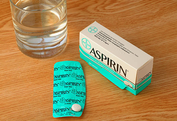 Bayer Aspirin tablet package with glass of water on table Idar-Oberstein, Germany - May 7, 2014: Bayer Aspirin tablet, containing 0.5 gram of acetylsalicylic acid as  active pharmaceutical ingredient, located on its blister pack with package and glass of water on table. Aspirin is one of the most common and used pharmaceutical drugs worldwide. In 1897 Aspirin was first synthesized by the german company Bayer. It was mainly used to relieve pain and aches, but today it is also known to help to lower the risk for strokes, heart attackes and maybe some type of cancer if taken in low dosis regulary. Aspirin should be taken with sufficient water. The pictured package is the one being sold in Germany. bayer schering pharma ag photos stock pictures, royalty-free photos & images
