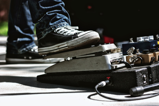 Guitarist wearing Converse Converse style shoes with his foot on a volume pedal at an outdoor performance.