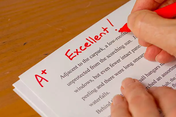 Photo of Hand and Red Pen Grading Papers with Excellent