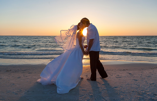 Bride and groom with leis and flower bouquet outdoors on the beach